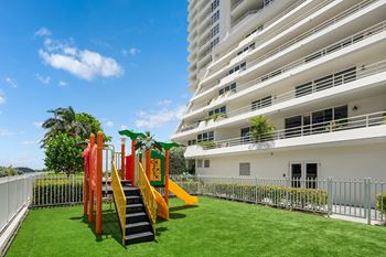 A playground with a slide and a climbing frame is in front of a white building.
